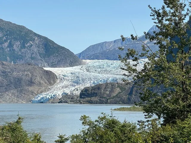 Mendenhall Glacier viewed across the lake, framed by green trees on the right.