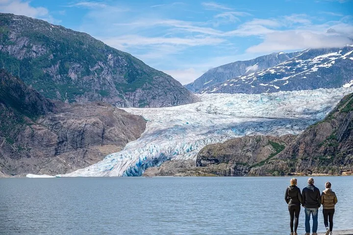 Turistas parados en la orilla mirando hacia el enorme Glaciar Mendenhall.