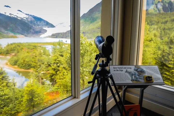 A spotting scope pointing out the window towards Mendenhall Glacier and lake.