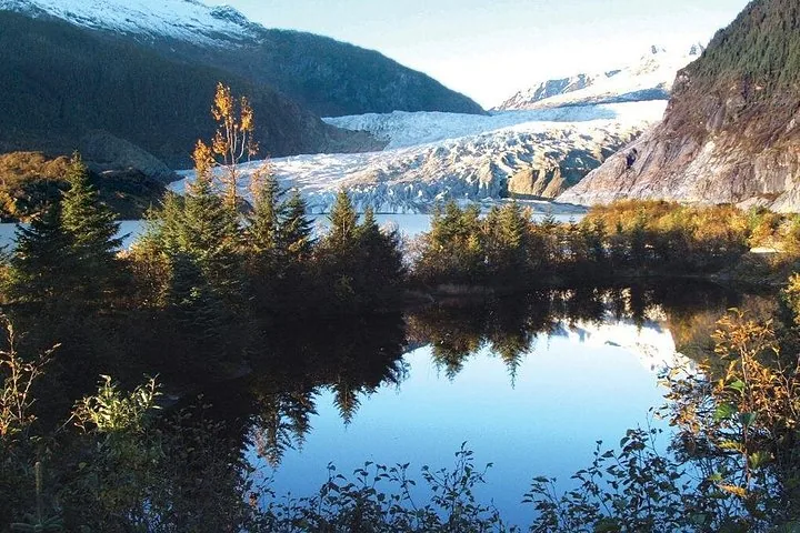 Glaciar Mendenhall reflejado en un estanque tranquilo rodeado de árboles otoñales.