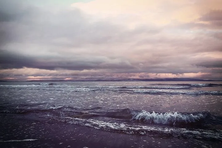Waves crashing onto a beach under a dramatic, cloudy sky at dusk.